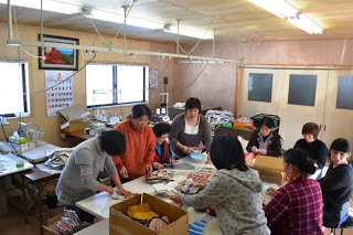 室内で数名の女性が手作業で布を扱い、製作活動をしている様子の写真