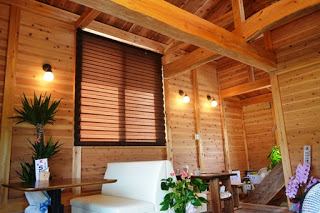 木製の壁と天井に囲まれた温もりのある部屋の中に、白いソファとテーブルが置かれ、観葉植物や花が所々に飾られている写真