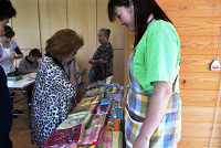 カラフルな布が置かれた机の前にエプロンを着けた女性が立ち、参加者の女性たちが興味深そうに布を選んでいる写真