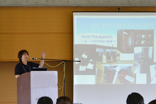 講演者の女性がマイクが設置された演台に立ち、隣のスクリーンに映されたスライドを使って発表を行っている写真