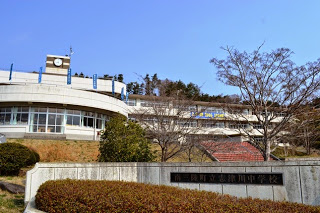 「南三陸町立志津川中学校」と書かれた看板が立っている校門の奥に立つ、3階建ての校舎が写っている写真