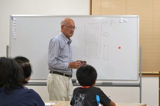 白いホワイトボードの前で男澤達夫さんが図を描きながら説明していて、複数の受講者が座って聞いている教室の様子の写真