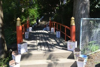 赤い欄干の小さな橋と両側に置かれた灯篭が見える参道の写真