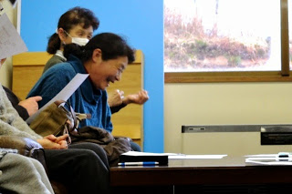 机に置かれた資料を見ながらひとりの女性が笑顔で座っている様子をアップで写した写真