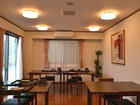 大きな窓があり、壁に額縁に入った絵画が飾られた室内に、四角い木のテーブルと椅子がいくつも並んでいる、落ち着いた雰囲気の食堂の写真