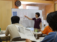 佐藤金枝先生がホワイトボードを指差しながら席に座っている受講生たちに説明をしている写真