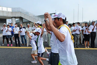 道路わきで応援している人たちの前を大人と子どもが手をつないで楽しそうに両手を上げて走っている様子を真横から写した写真