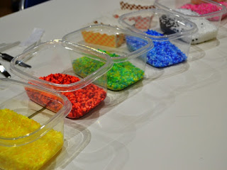 透明なプラスチック容器に入った赤・青・黄など色とりどりのビーズがテーブルの上に整然と並べられており、手芸や工作の準備がされている様子を写した写真