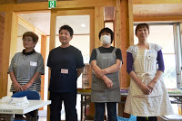 名札をつけエプロンや作業着を着た4人のスタッフが横一列並んで立っている写真