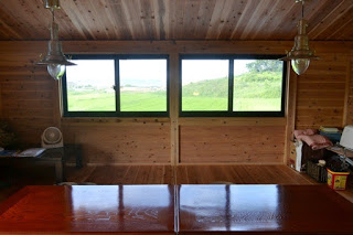 木造の部屋の中にテーブルが置かれ、窓からは緑豊かな外の風景が見えている写真