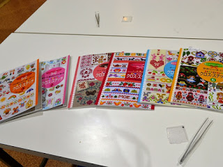 白いテーブルの上に6冊のクロスステッチの本が並べられており、それぞれの表紙には異なるデザインや色彩の刺繍作品が描かれている様子を写した写真