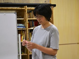 室内の本棚の前で、手に持ったアイロンビーズを見ながら立っている鈴木ルミ子さんの写真