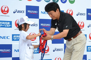 男性と女の子が赤や青のタスキの受け渡しをしている写真