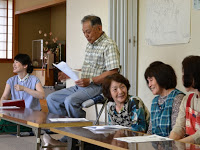 男性が椅子に座り、周囲の女性たちが楽しそうに話を聞いている写真