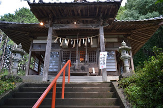 石灯篭としめ縄が飾られた木造の拝殿が階段の上に立ち、拝殿の正面には赤い手すりが見える山の中の神社の写真