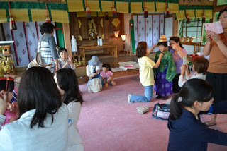 神社の室内に多くの人が集まり、子どもたちに衣装や髪飾りをつけたり、大人が見守ったりしている和やかな雰囲気の準備の様子の写真