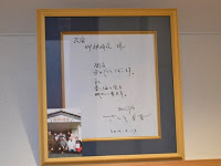 直筆のメッセージが描かれた色紙と、宿泊施設の前でスタッフ々が並んで写っている集合写真が一緒に額に入って飾られている写真