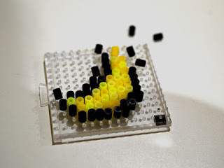 たくさんの突起が付いた透明な四角いプレートの上に黄色と黒のビーズが並べられ、三日月の形に丁寧に配置されている様子を写した写真