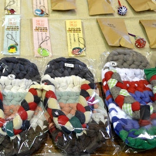 色とりどりの布で編まれた草履が透明な袋に入れて並べられ、その上には包装された小物やストラップが整然と置かれている写真