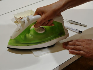 ビーズの上にクッキングシートを乗せ、黄緑色のアイロンをあてている手元を写した写真