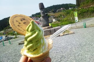 屋外で本物のモアイ像を背景に、モアイソフトを手に持って撮影した写真