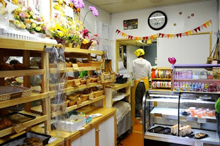 店内で、木製の棚にさまざまな焼き菓子が陳列され、奥ではスタッフが作業しており、冷蔵ショーケースにはケーキやゼリーが並んでいる写真