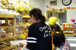 店内で、トレイとトングを持ってパンや焼き菓子を選んでいる女性が写っており、棚には焼きたての焼き菓子、パンが並べられている写真