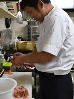 白い調理服を着た料理人の男性が、台所でエビの皮をむいている調理中の写真