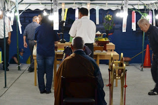 テントの中に設けられた祭壇にお参りをする人々と、後方に座った僧侶の後ろ姿が写っている写真