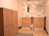 左の壁側に収納棚があり、鏡の上に白い照明がついている木目調の洗面台が二つ並んでいる洗面所の写真