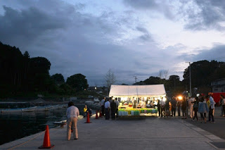 空が暗くなりはじめ、ライトで煌々と照らされたテントの周りに多くの人々が集まっている様子を写した写真