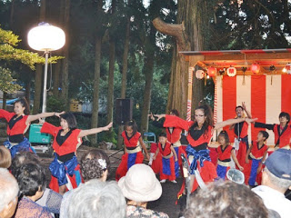 赤と黒の衣装を着た女性たちがライトに照らされながら、舞台の前で躍動的に踊っている写真