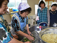 まわりの女性たちが手元を見守っているなか、参加者の女性が水を出しながら野菜を洗っている写真