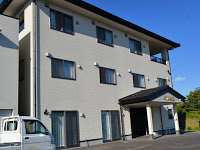 オフホワイトの三階建ての建物を斜めから捉え、玄関に黒い瓦屋根の庇がある民宿「明神崎荘」の外観写真