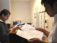 事務所内で、佐々木さんと料理長が紙を見ながら打ち合わせをしている写真