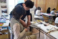 男性スタッフが女性の手元を見ながら丁寧にサポートし、布を伸ばす作業を手伝っている写真