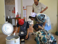 3人の参加者がのぞき込んで見ているなか、赤い三角巾をつけた男子スタッフがお椀によそいだご飯を計量している写真