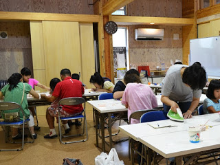 各テーブルで子どもと大人が混ざり、アイロンビーズのストラップ作りをしている写真