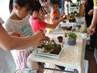子供たちが屋外で植物を植えるワークショップに参加しており、土に触れながら苗を丁寧に植えている様子が写っている写真