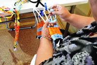 参加者がハンガーに布のような素材を巻きつけてオレンジ色と水色の布を編む作業を進めている写真