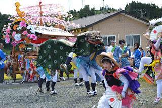 神輿の前で獅子舞をしている人々と踊る子どもが一緒にいる様子の写真