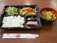 ごはん、2種類の野菜を使ったおかず、水ようかん、スープが入った健康的な手作り弁当が箸と共にテーブルに置かれている写真