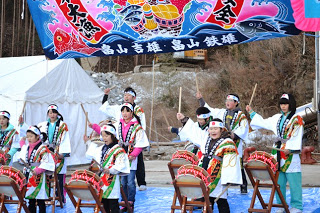 法被を着た子どもたちが屋外ステージで太鼓を叩き、背景には大漁旗が掲げられている寄木ささよの太鼓演奏の写真