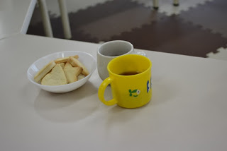 白いテーブルの上に、星やハートの形のクッキーが入った白い皿と、飲み物が入った白いマグカップ、黄色コップが置かれている写真