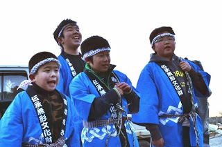 青い法被を着た4人の男の子たちが歌を歌っている様子の写真