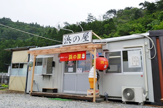 店頭には赤い提灯とソフトクリームの模型があり、「浜の屋」と書かれた看板があるプレハブ造りの飲食店の写真