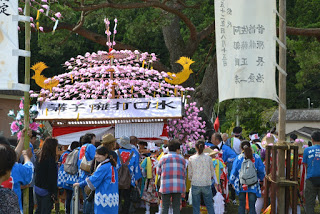 人々が華やかな桃色の装飾の神輿に向かって歩いている祭りの風景の写真