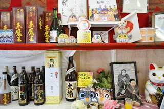 棚に焼酎のボトルや招き猫、フクロウの置物などが並べられた店内の写真