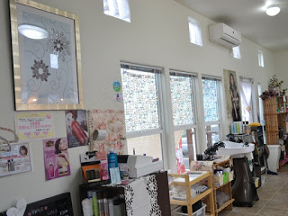 大きな窓から光が差し込む明るい室内に美容グッズが並び、シャンプー台も見える美容室内の写真