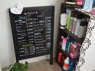 整頓された美容用品の棚がある手前の壁際に設置された、男性用と女性用のメニューと料金がびっしりと書かれた黒板の写真